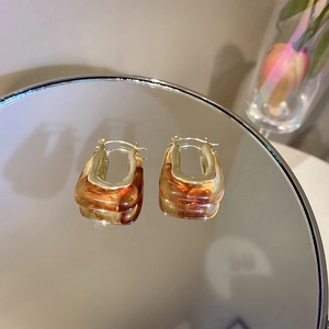 Close-up of gold U-shaped earrings with amber resin on a reflective mirror base
