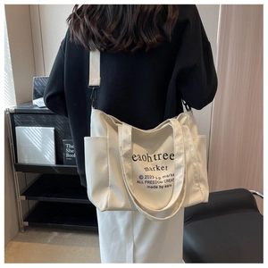 Detailed view of cream canvas tote bag with black printed text and adjustable strap