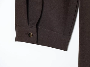 Detailed close-up of dark brown shirt sleeve with woven texture and gold metal button