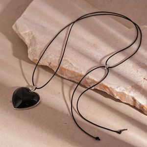 Close-up of black heart pendant necklace with silver trim on a textured stone surface