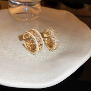 Detail of gold-plated open rings with pearls and zircons on a white ceramic plate