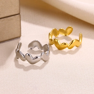Close-up of heart-linked open rings in gold and silver finish on a textured background