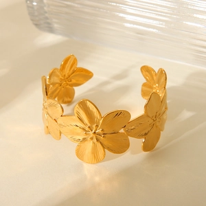 Elegant gold floral stainless steel open bangle displayed on a textured beige surface