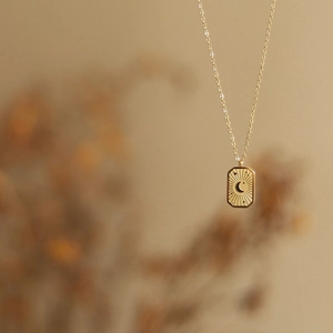 Vue macro d'un pendentif carré plaqué or avec motif gravé de rayons de soleil et lune