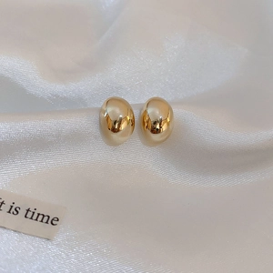 Detailed close-up of golden bean-shaped stud earrings on white silk texture background