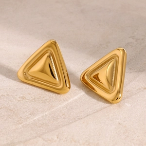 Vue macro des boucles d'oreilles triangles dorées en acier inoxydable sur pierre