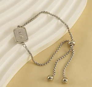 Detail of silver S letter pendant on adjustable box chain bracelet with textured background