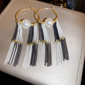 Close-up of golden flower stud earrings with white pearl and long metallic tassels