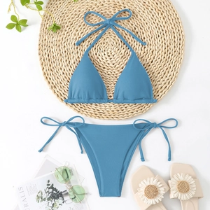 Flat lay of gray blue ribbed triangle bikini set with straw mat and summer accessories