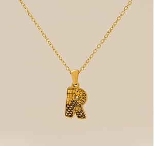 Détail du collier pendentif lettre R doré avec des textures de gravure bohème