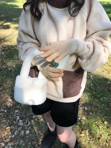 Outdoor lifestyle shot of beige knit gloves and a white plush handbag in natural light
