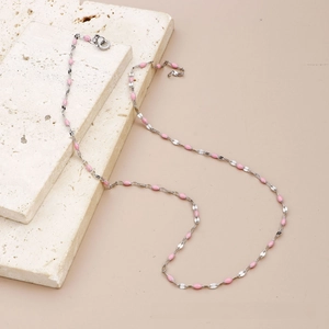 Detail of silver chain necklace with pink enamel beads on textured stone display