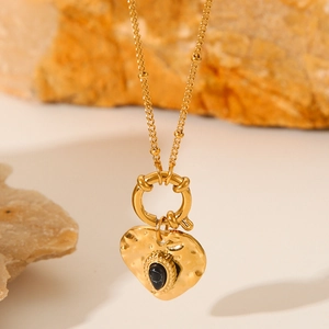 Detail of gold heart necklace with hammered texture and black gemstone on natural rock