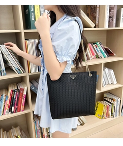 Detail of black woven texture tote bag with metal chain strap and triangular logo plate
