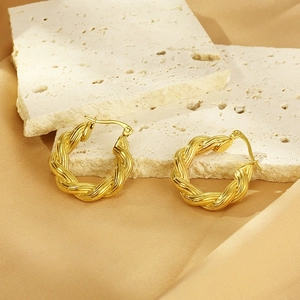 Macro detail of gold-plated twisted rope hoop earrings on champagne silk and stone