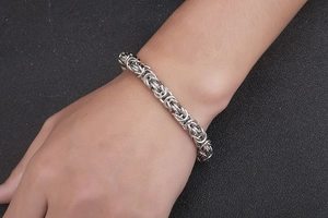 Close-up of a silver Byzantine weave stainless steel bracelet on a male wrist
