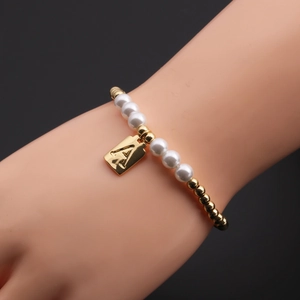Detail of beaded pearl bracelet with gold letter A pendant worn on model wrist