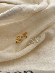 Detailed view of gold and silver GOOD letter hoop earrings on textured white fabric