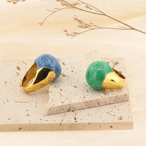 Detail of chunky gold rings with blue and green marble resin domes on stone surface