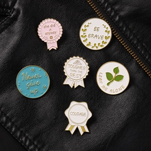 Detail of six enamel pins with motivational quotes displayed on black leather background