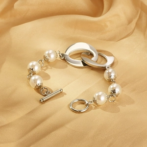 Macro view of interlocking silver rings and pearl strand on silk fabric with T-bar clasp