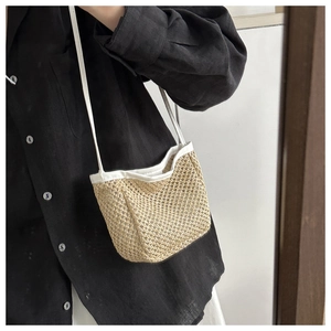 Detail of straw crossbody bucket bag featuring natural fiber weave and white strap
