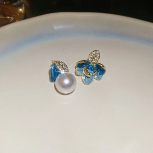 Macro shot of asymmetrical blue enamel flower and pearl earrings with cubic zirconia