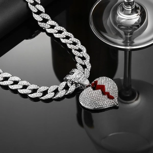 Dettaglio catena cubana con ciondolo a cuore e fulmine rosso su riflesso a specchio