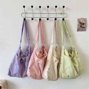 Detail of waffle-textured canvas shoulder bags with bird embroidery in four pastel colors