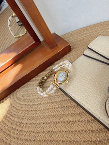 Detailed shot of retro oval gold watch with double-row pearl strap on beige background