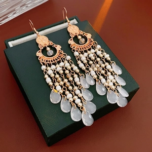 Ethnic teardrop tassel earrings with white beads and gold filigree on a jewelry box