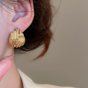 Detail view of vintage golden metal stud earrings with a 3D wavy ripple texture design