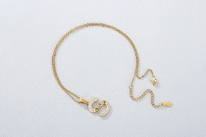 Detail of gold S-shaped pendant with rhinestones and SMILE engraving on a cable chain