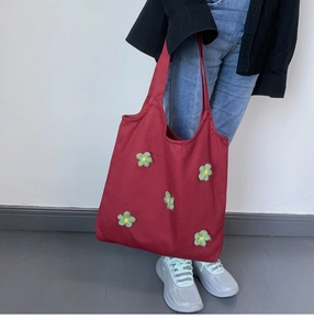 Detail of red canvas tote bag with yellow and green knitted floral accents being carried