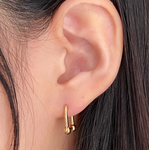 Close-up of geometric gold U-shaped link earrings with ball ends on model ear