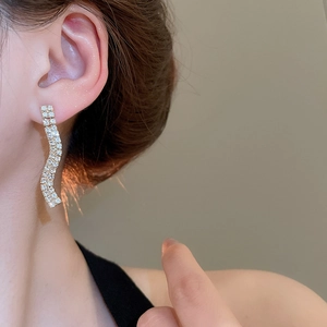 Close-up of elegant gold S-curve wavy earrings with sparkling diamonds on female model