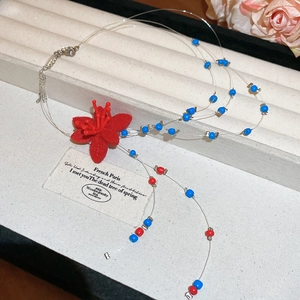 Detail of beaded necklace with blue and red beads and a large red flocked flower charm