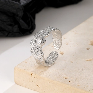 Macro detail of irregular textured silver open ring with round clear gemstone on stone