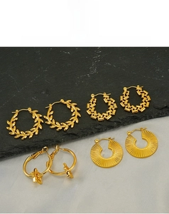 Detail view of five different vintage gold star and leaf earrings on grey silk and stone
