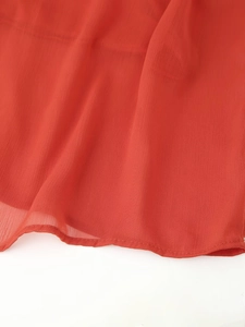 Detailed close-up of the fine mesh fabric and stitched hem of the red ruched dress