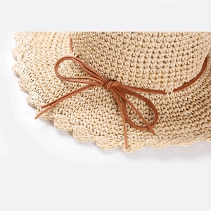 Détail du chapeau de soleil en paille tissé à la main avec bord ondulé et nœud brun