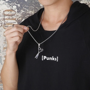 Détail d'un collier pendentif ciseaux argenté porté sur un sweat à capuche noir