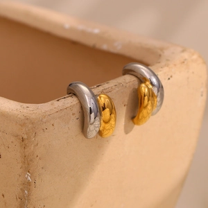 Detail of two-tone gold and silver curved stainless steel earrings on a ceramic bowl