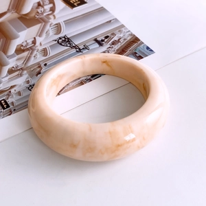 Dettaglio del bracciale in resina con trama marmorizzata crema su rivista di moda