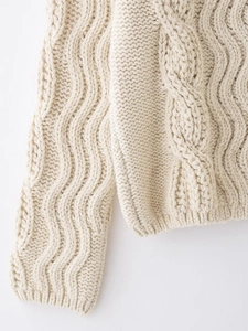 Close-up of cream cable knit wool sweater showing thick textured patterns and stitching