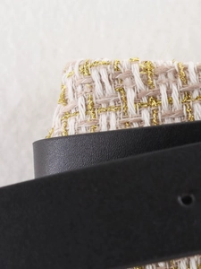 Macro shot of beige tweed fabric with gold threads and a black leather belt detail