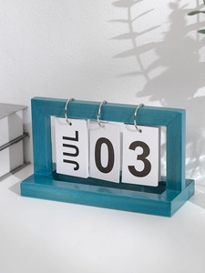 Macro view of teal wooden flip calendar with metal rings on a desk with natural shadows