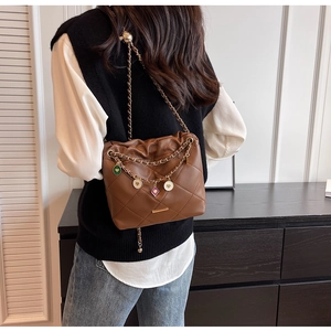 Close-up of brown quilted bucket bag with colorful enamel heart charms and chain strap