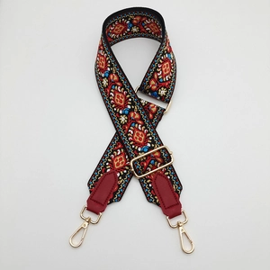 Close-up of ethnic embroidered canvas bag strap with red leather ends and gold metal hooks
