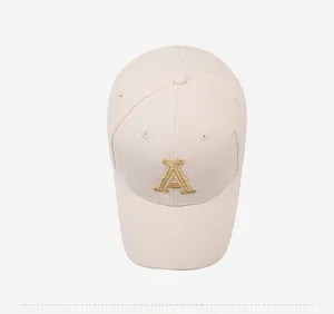 Top view of beige baseball cap with gold embroidered letter A and stitched eyelets